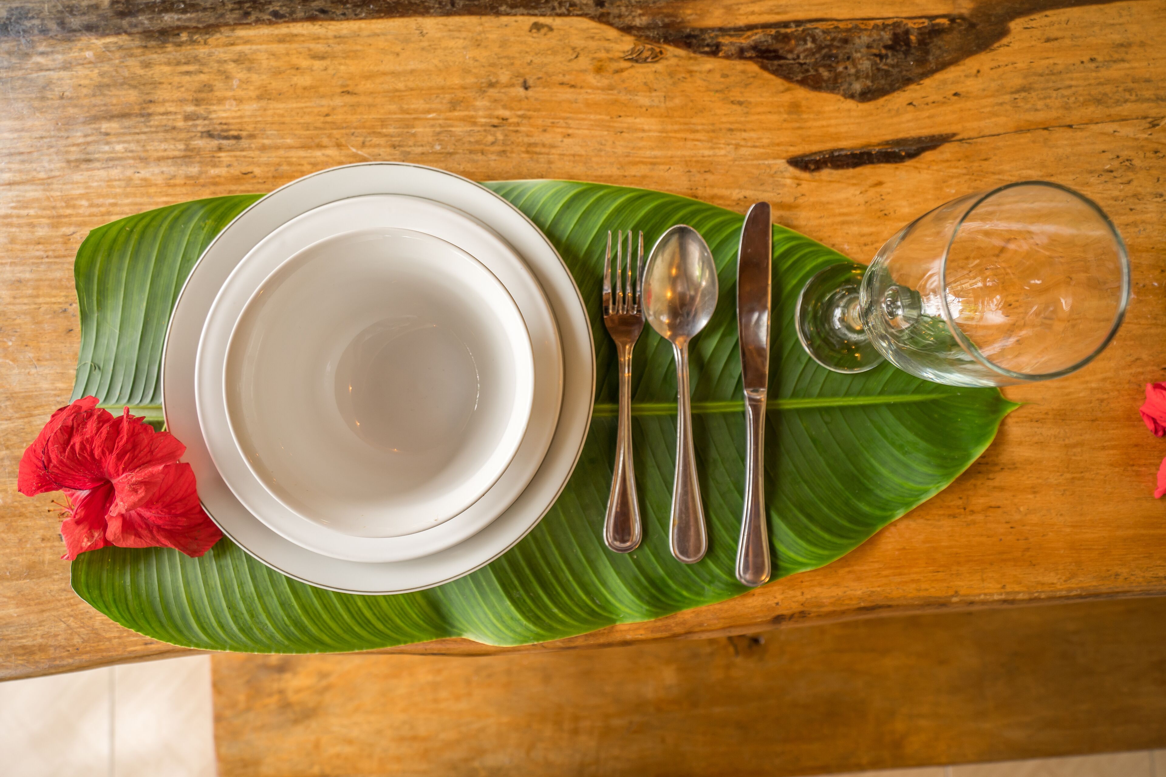 A table set with white plates, silver cutlery, and a glass on a green leaf.