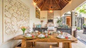 A dining area with a wooden table set for four, surrounded by a decorative wall with floral carvings. - Villa Mia And Spa (Seminyak)