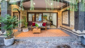 A lobby with a stone floor, a sofa with red cushions, and potted plants. - Villa Mia And Spa (Seminyak)