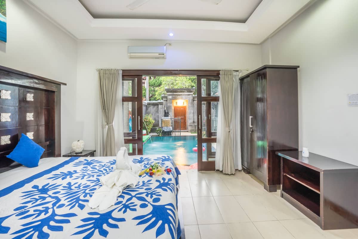 A hotel room with a bed, a TV, a wardrobe, and a view of a swimming pool.