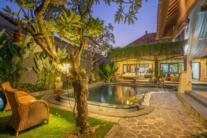 A pool area with a stone pathway, wicker furniture, and lush greenery.
