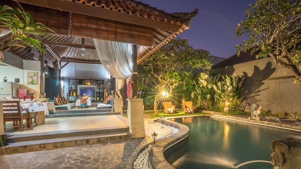 A pool area with a stone deck, a covered seating area, and a view of the pool. - Villa Mia And Spa (Seminyak)