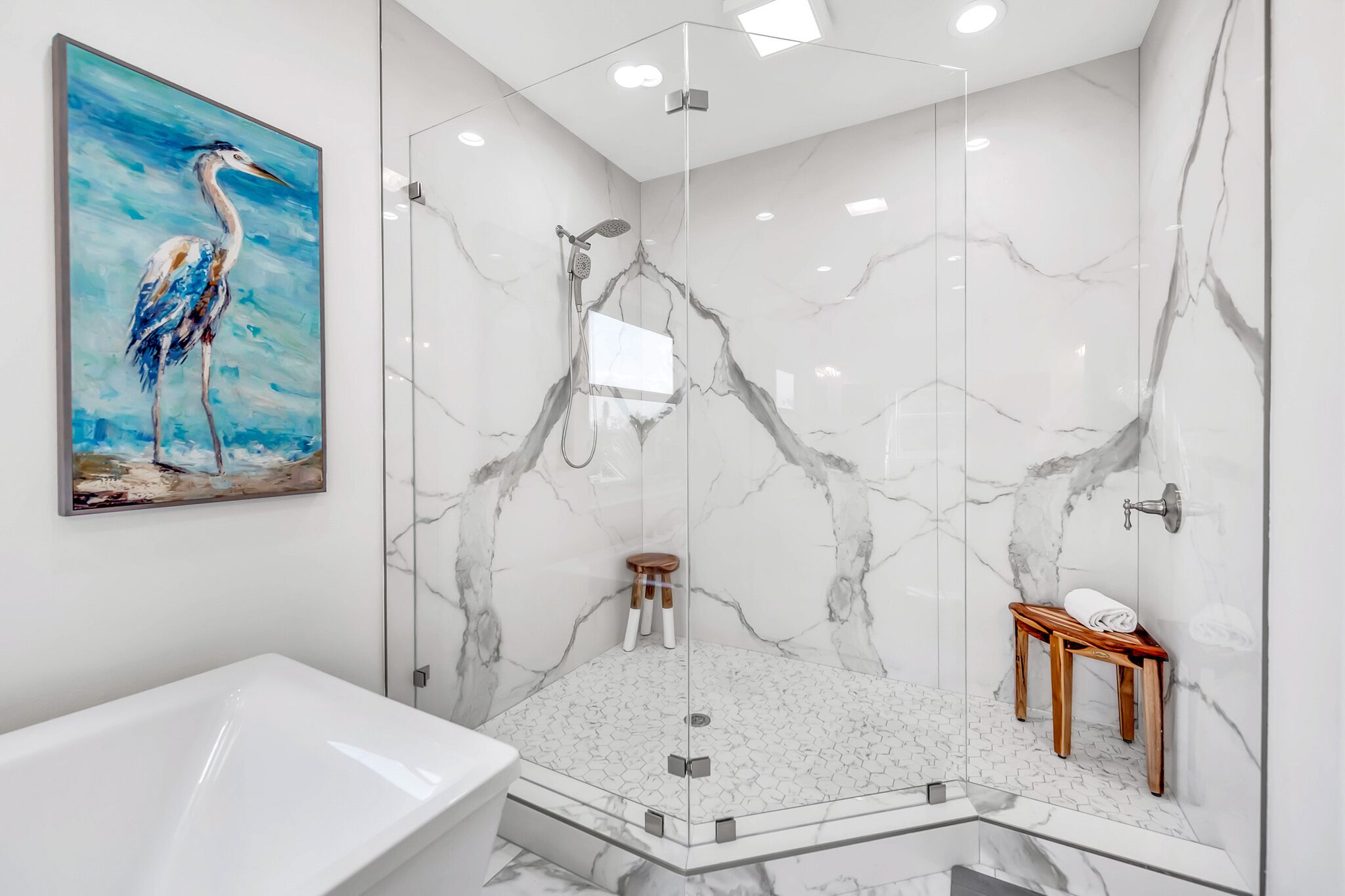 Un baño moderno con ducha envuelta en vidrio, una bañera blanca y un banco de madera.