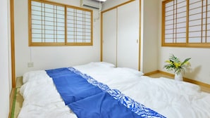 A traditional Japanese-style room with tatami flooring, a bed with a blue and white bedspread, sliding doors, and a small potted plant. - Guest House Asato (Naha)