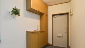 A small, enclosed room with wooden cabinets, a tiled floor, and a door with a towel hanging on it. - Guest House Asato (Naha)
