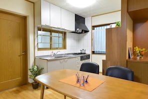 A compact kitchen with white cabinets, a black range hood, and a window above the sink. - Guest House Asato (Naha)