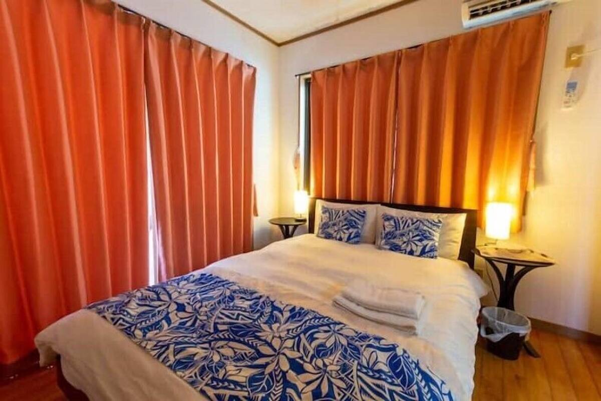 Una habitación de hotel con una cama grande, dos mesitas de noche, aire acondicionado instalado en la pared y cortinas.