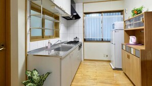A compact kitchen with a stainless steel sink, a microwave, and wooden cabinets. - Guest House Asato (Naha)