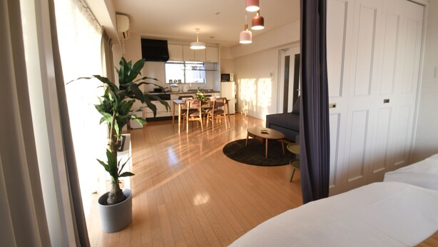 Een moderne hotelkamer met een houten vloer, een bed, een zithoek en een keuken op de achtergrond.