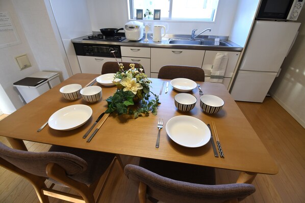 Een eettafel gedekt met borden, stokjes en een bloemstuk, in een moderne keuken met een raam en inbouwapparatuur.