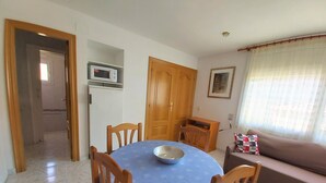 A dining area with a round table covered in a blue tablecloth, surrounded by wooden chairs. A microwave is mounted on the wall above the table. - Colera Apartment B in Costa brava (Colera)