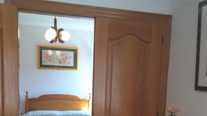 A bedroom with a bed, a wooden wardrobe, a small table with a vase, and a ceiling light fixture. - Colera Apartment B in Costa brava (Colera)