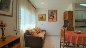 A living room with a sofa, a dining table with chairs, a wooden cabinet, and a vase with flowers. - Colera Apartment B in Costa brava (Colera)