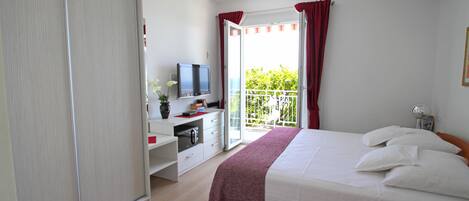 A bedroom with a bed, a TV, a desk, and a balcony with red curtains.
