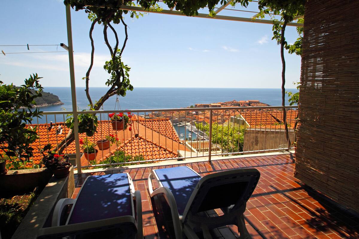 A terrace with lounge chairs, a view of the sea, and terracotta rooftops.