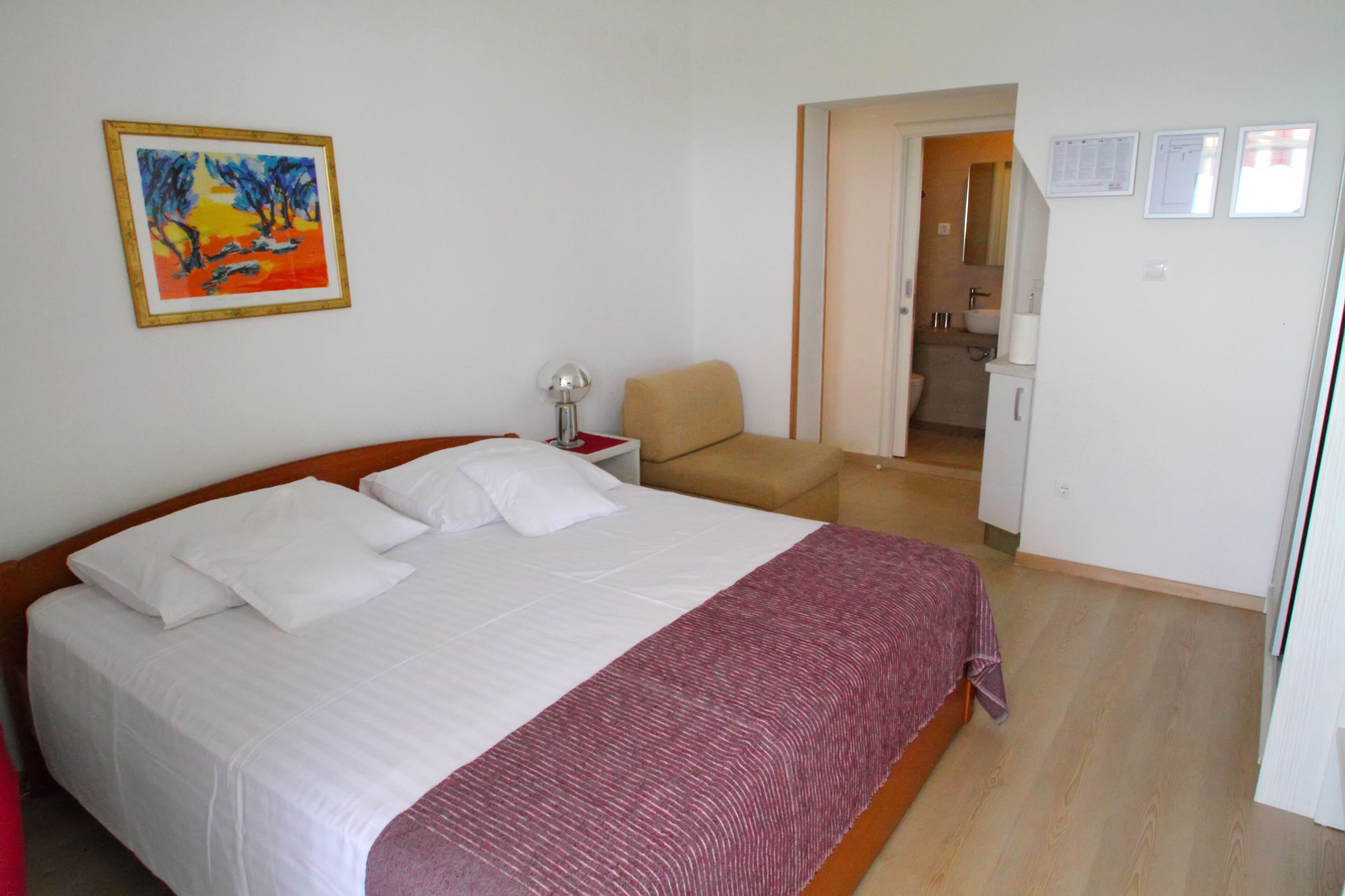 A bedroom with a large bed, a chair, a nightstand, and a painting on the wall.