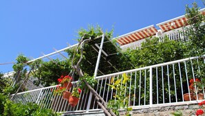 Un balcon en métal blanc orné de plantes en pot et de fleurs rouges.