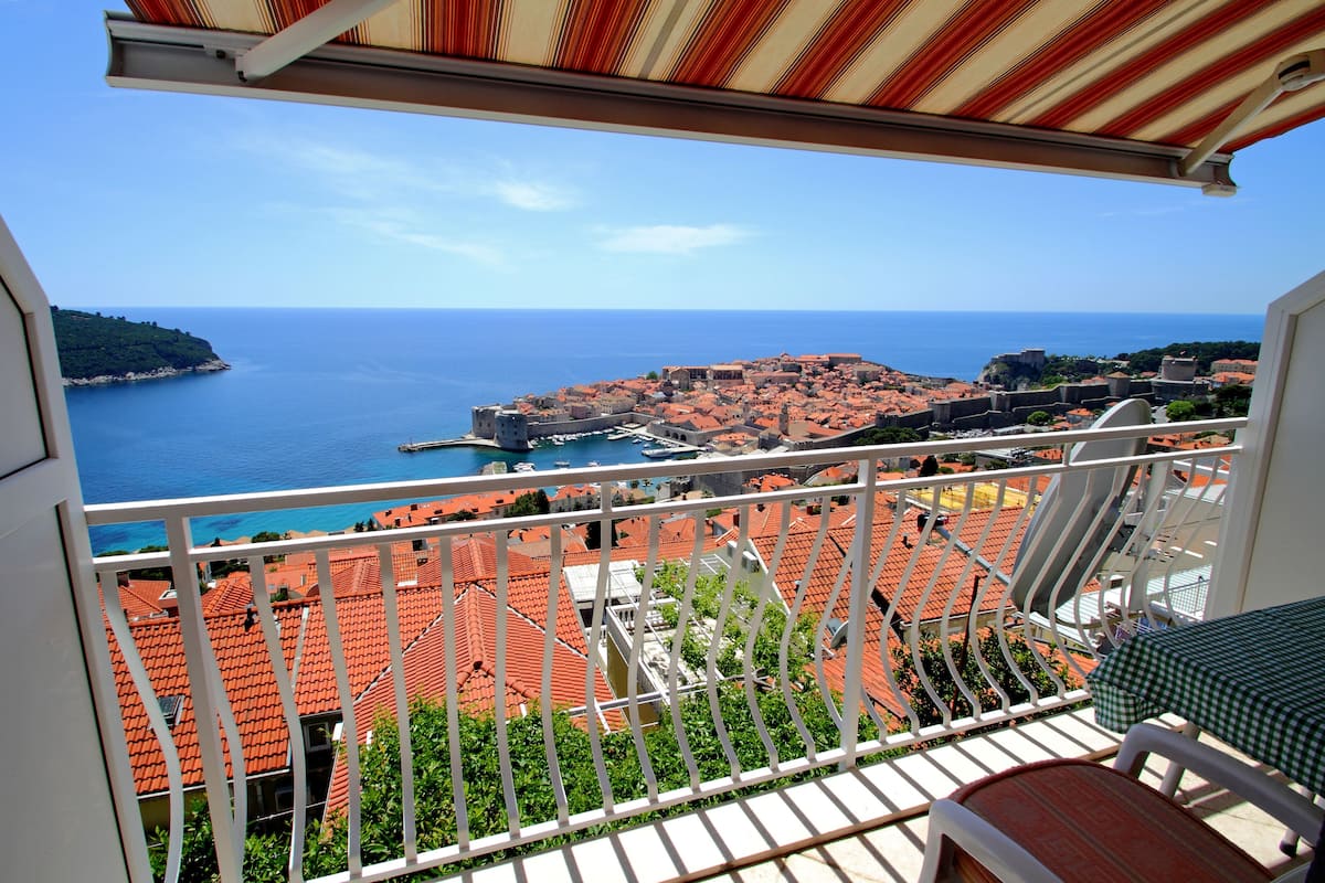 A balcony with a view of a coastal town, a table, and a chair.