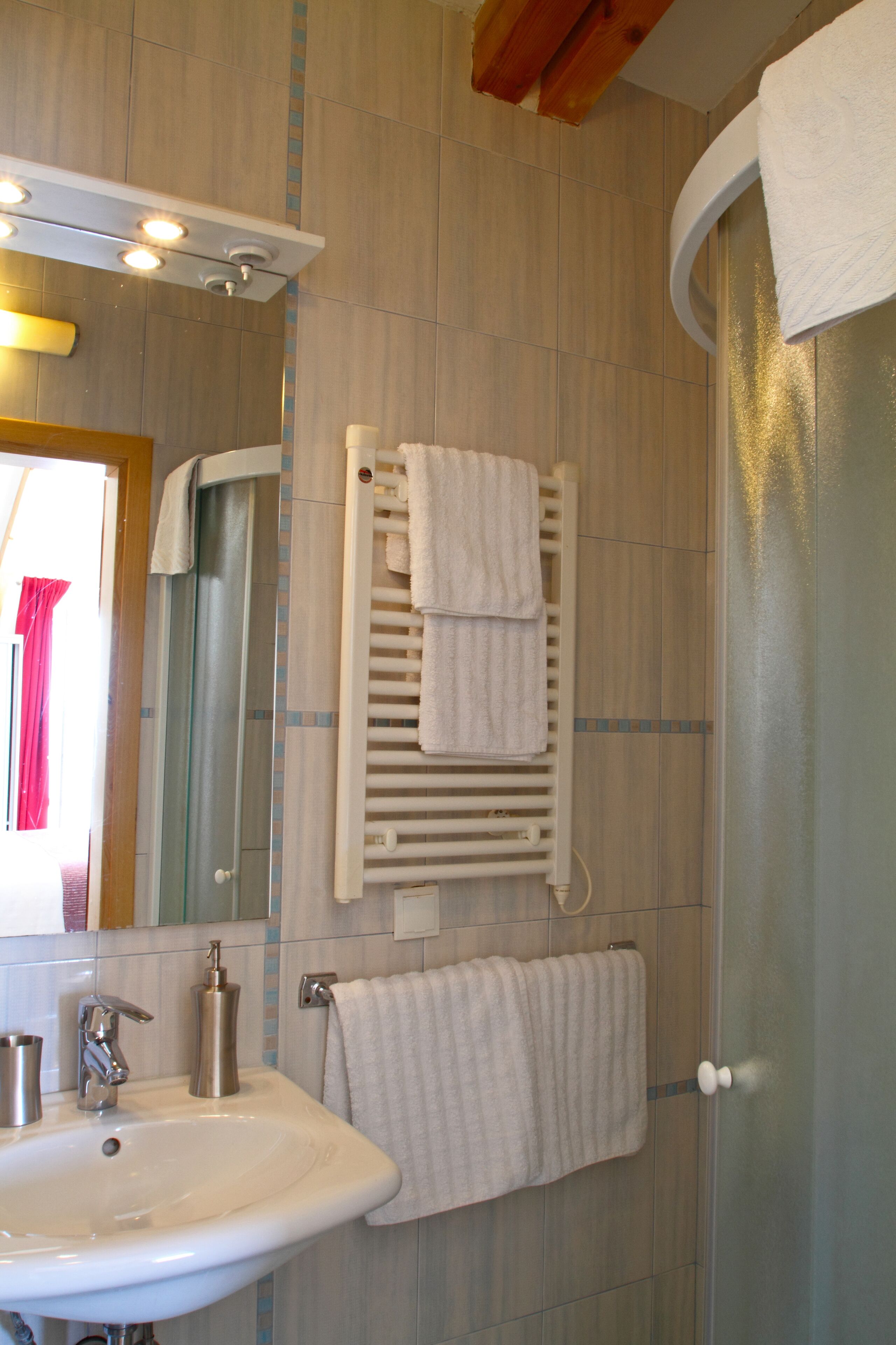A bathroom with a sink, mirror, towel rack, and a shower area.