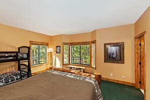 Habitación con literas, una cama grande, un escritorio y ventanas con vistas a árboles.