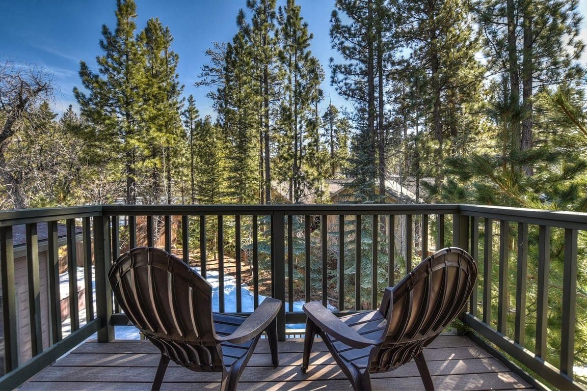 A deck with two chairs facing a pool, surrounded by tall trees.