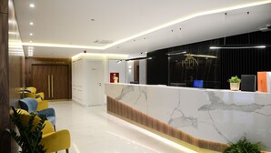 Zona de recepción de hotel con mostrador de mármol, una sala de conferencias y asientos con plantas en macetas.