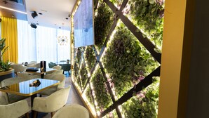 Un comedor moderno con una mesa de vidrio, sillas acolchadas y una pared jardín vertical.