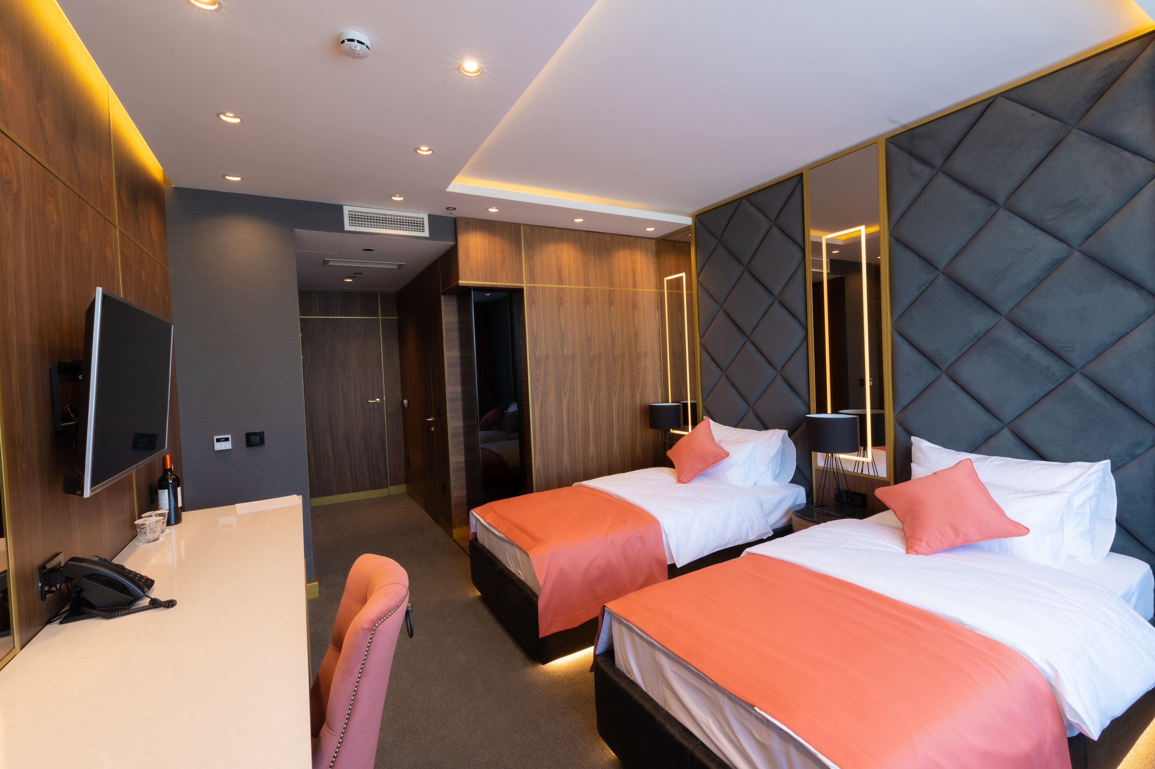 Habitación de hotel con dos camas, un escritorio, una silla y un espejo grande.