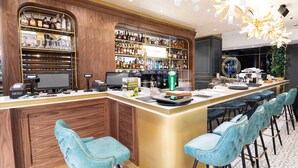 Zona de bar con mostrador de madera, estantes con botellas de licores, una caja registradora y taburetes de bar azules.