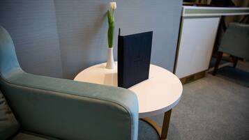 Habitación de hotel moderna con una silla tapizada de verde, una mesa redonda blanca y una libreta o carpeta negra.