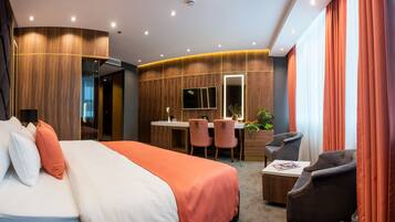 A modern hotel room with a large bed, a desk with two chairs, a TV, and a small table with a magazine.