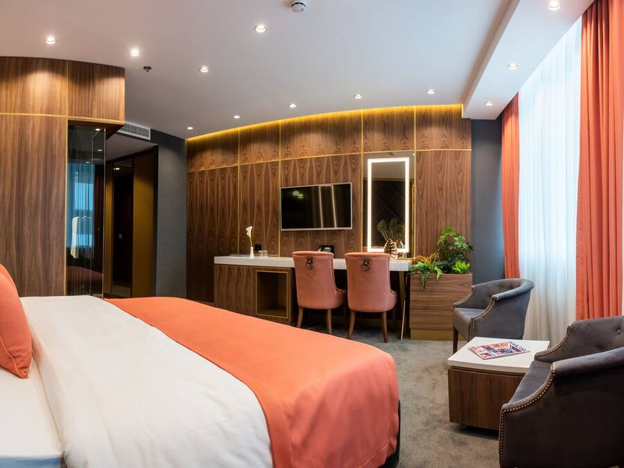 A modern hotel room with a large bed, a desk with two chairs, a TV, and a small table with a magazine.