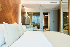A modern hotel room with a large bed, a seating area with a sofa and a small table, and a view through a glass door. - Hotel Pupin (Novi Sad)
