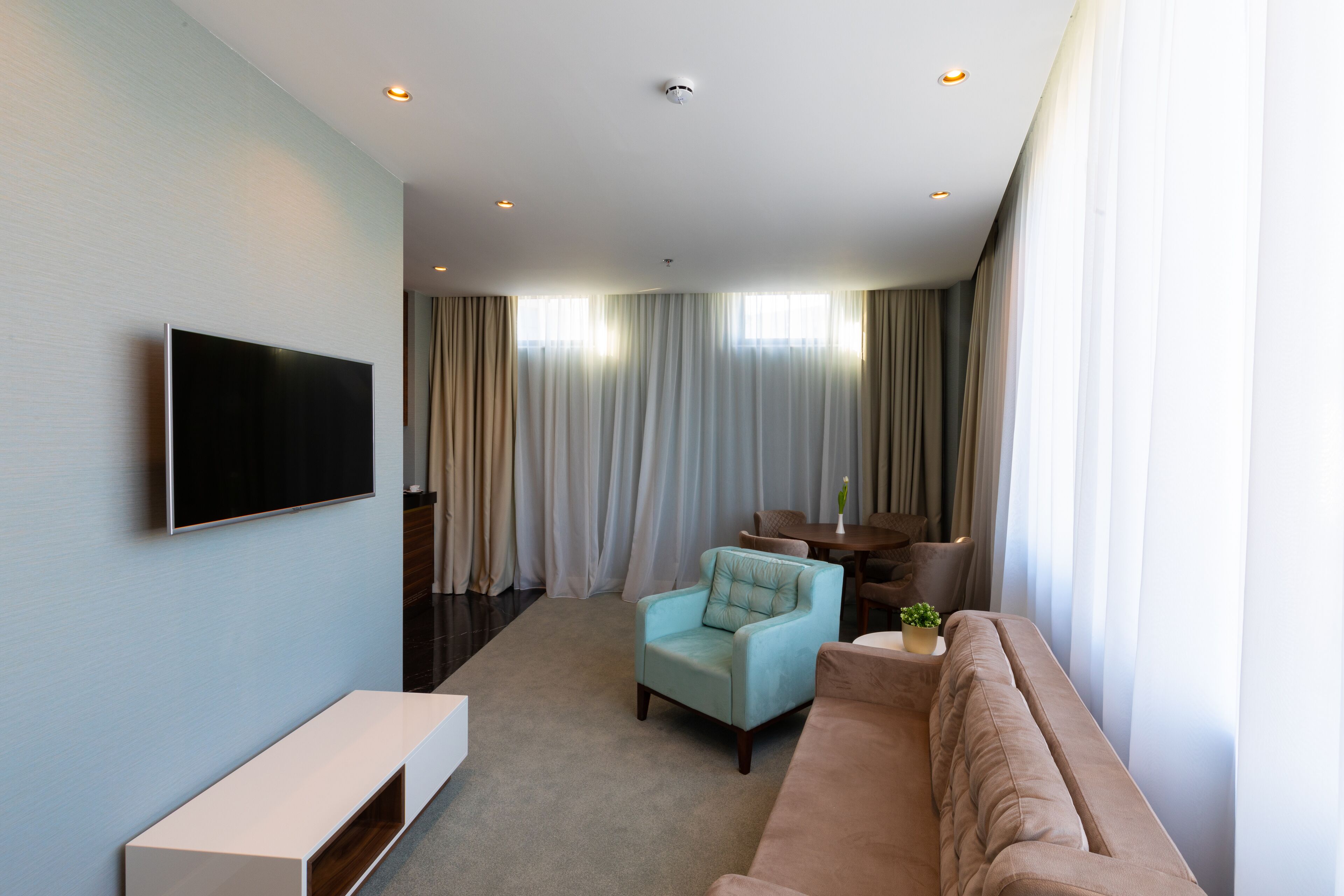 A modern living room with a flat-screen TV, a beige sofa, a light blue armchair, and a small table with a plant.