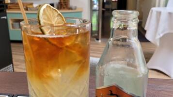A glass of iced tea with a lemon slice, a bottle of Goldberg ginger beer, and a black and white patterned tablecloth.