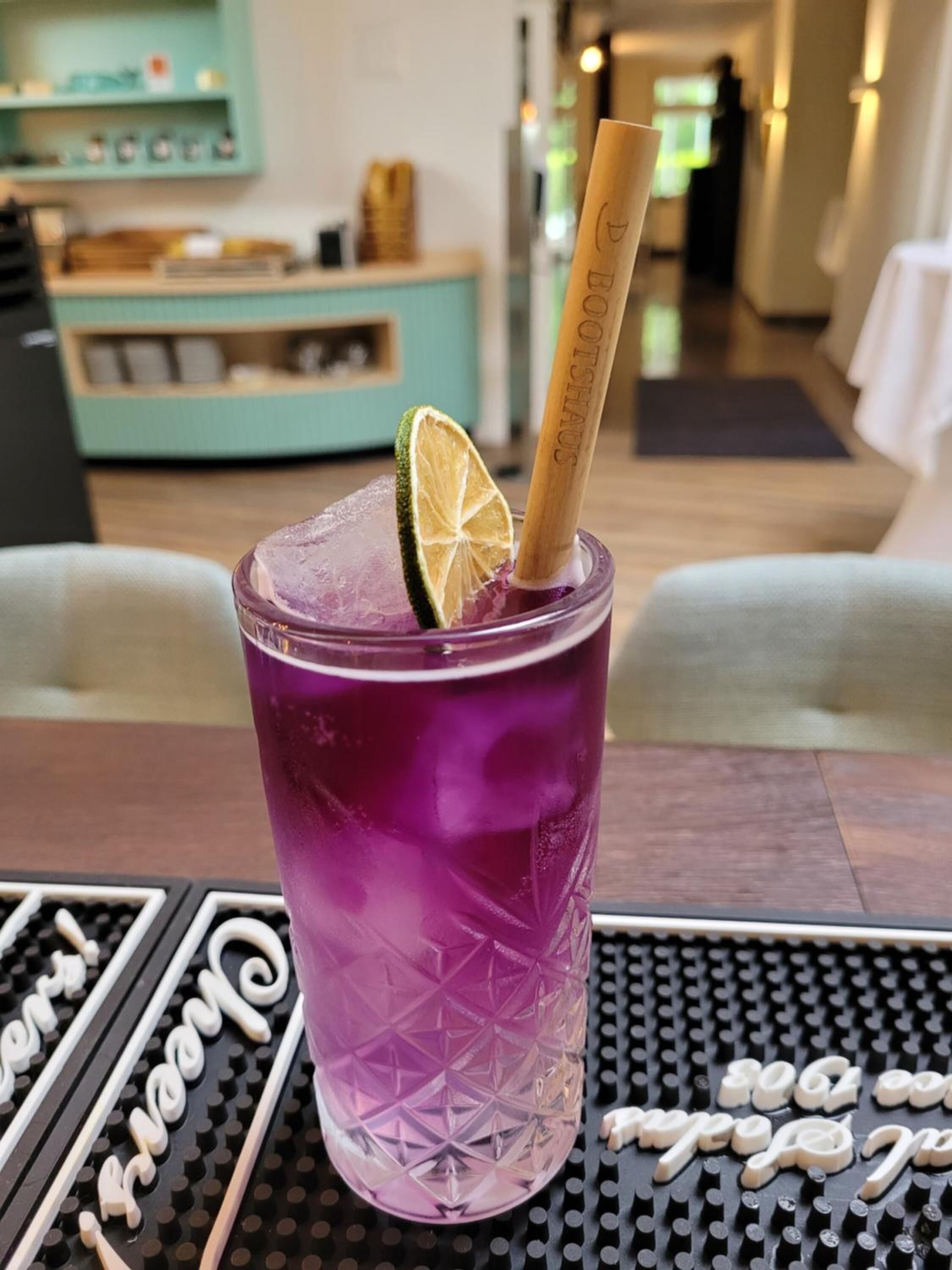 A purple drink with a lime slice and a straw in a textured glass, placed on a black table with white text.