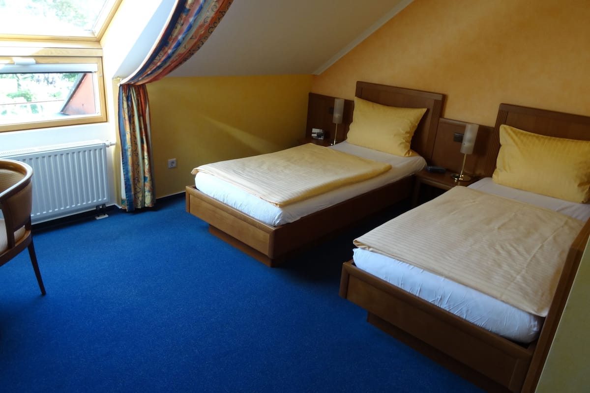A room with two beds, a chair, a window with curtains, and a radiator.