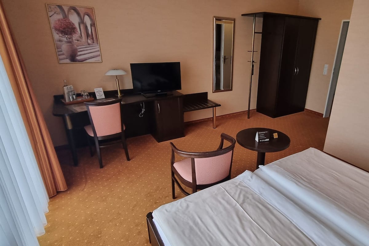 A hotel room with a bed, a desk with a television, a chair, a wardrobe, and a small table.