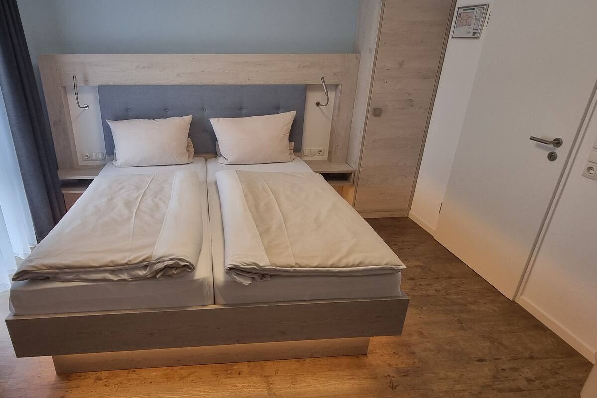 A double bed with two pillows, a wooden headboard, a small bedside table, and a wardrobe with a mirror.