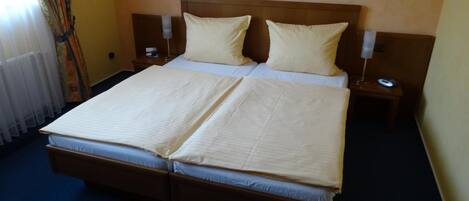 Una cama doble con dos almohadas, una mesita de noche con lámpara y una ventana con cortinas.