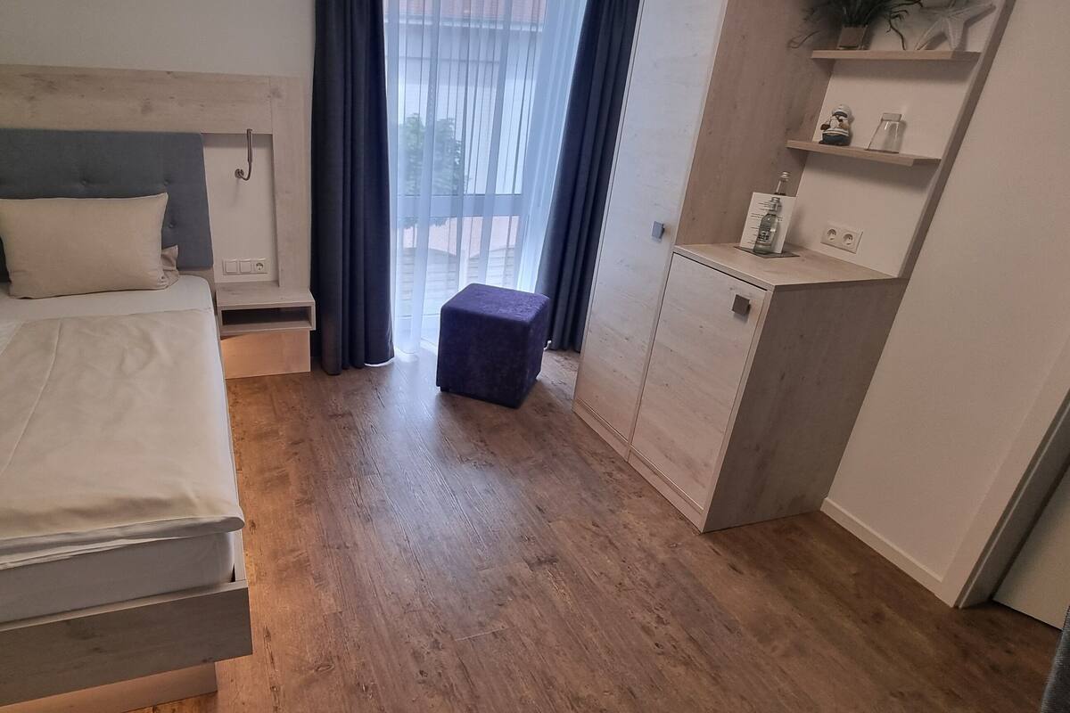 A bedroom with a bed, a nightstand, a small table, a wardrobe, and a window with curtains.