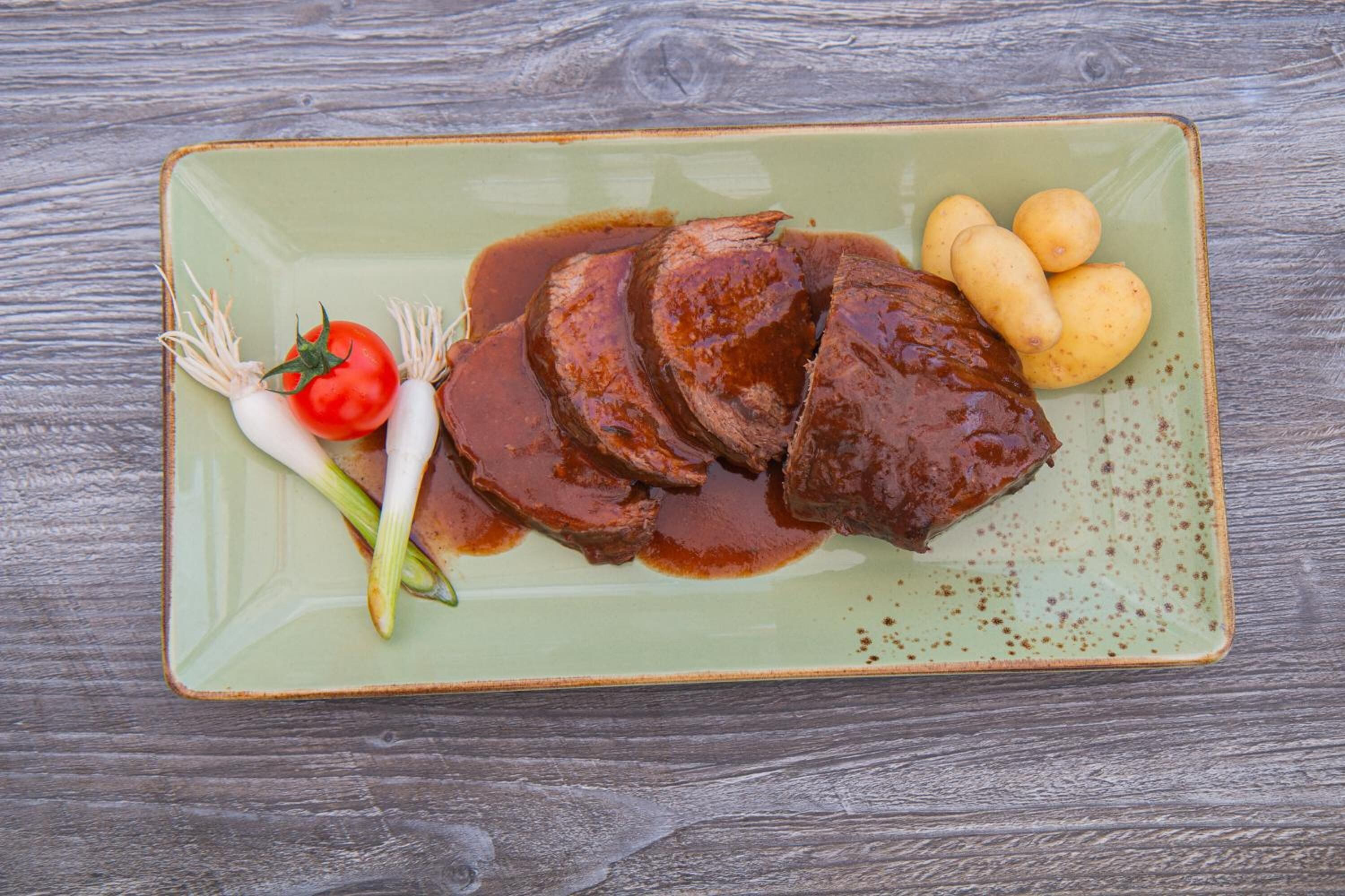 Un plato con carne en rodajas, patatas y verduras sobre una mesa de madera.