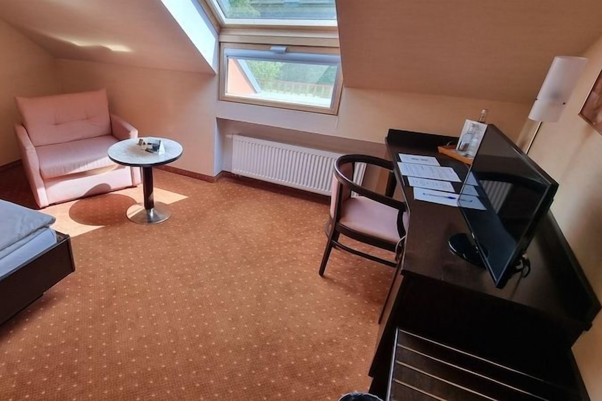 Habitación de hotel con cama, escritorio, silla, mesita y ventana.
