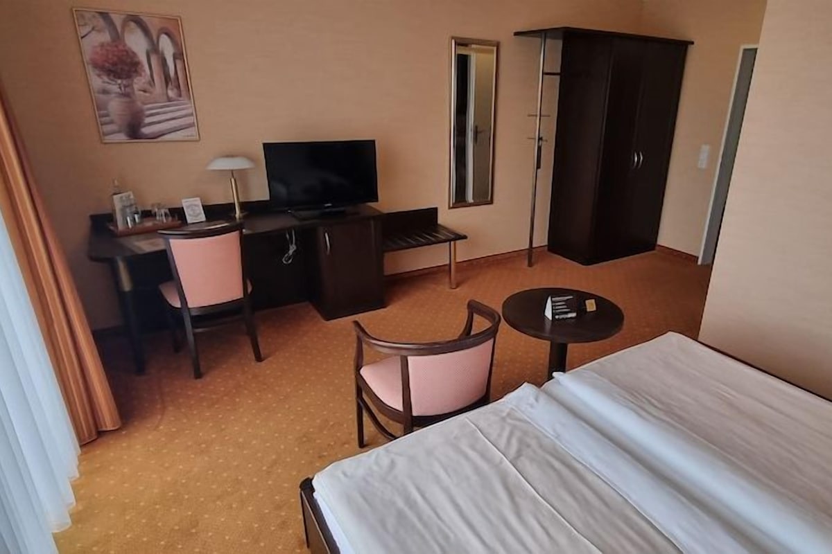 Una habitación de hotel con una cama, un escritorio con una silla, televisión, armario y una mesita.
