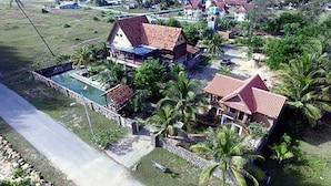 A residential area with a house featuring a swimming pool, surrounded by palm trees and a small garden. - Kijalena Beach BnB (Kijal)