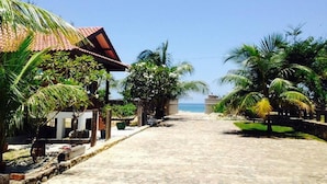 A paved pathway leading to a beach, flanked by palm trees and a building with a red-tiled roof. - Kijalena Beach BnB (Kijal)