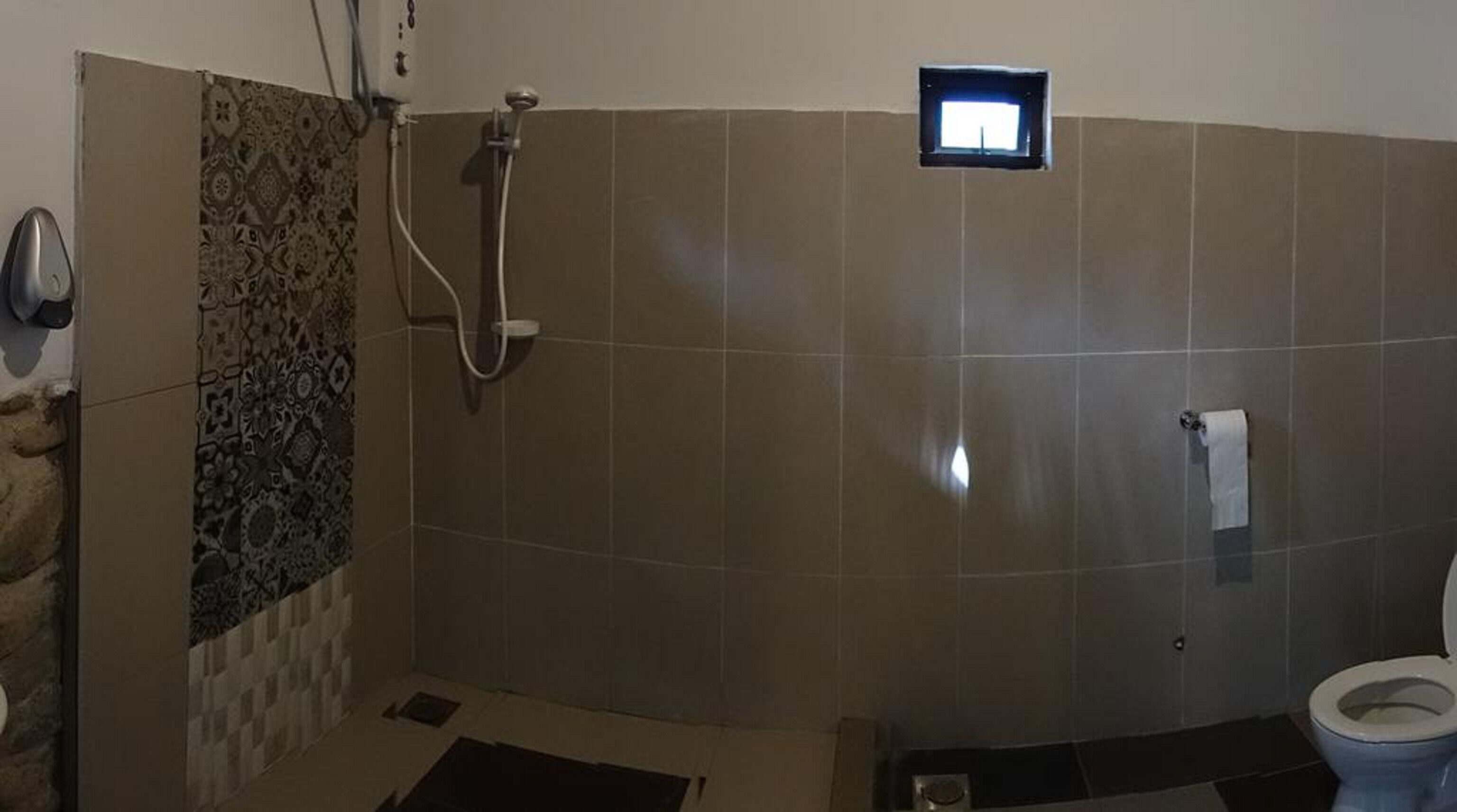 A bathroom with a shower, toilet, and a small window.