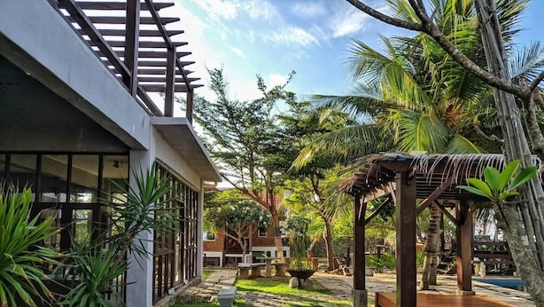 A modern building with a stone pathway leading to a covered seating area surrounded by lush greenery and palm trees. - Kijalena Beach BnB (Kijal)