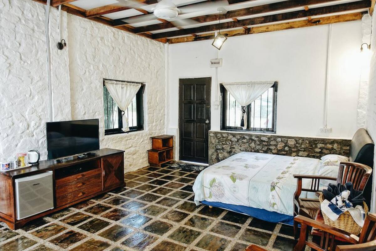 A bedroom with a bed, a TV, a dresser, and a small refrigerator.