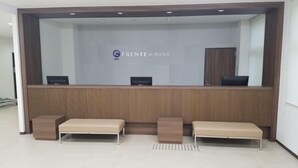 A reception area with a wooden reception desk, two cushioned benches, and a wall-mounted TV. - Hotel Frente Hirono (Hirono)
